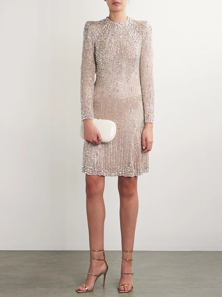 Model wearing a beaded long sleeve mini dress with a clutch and gold heels.