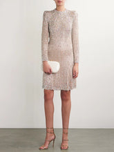 Model wearing a beaded long sleeve mini dress with a clutch and gold heels.