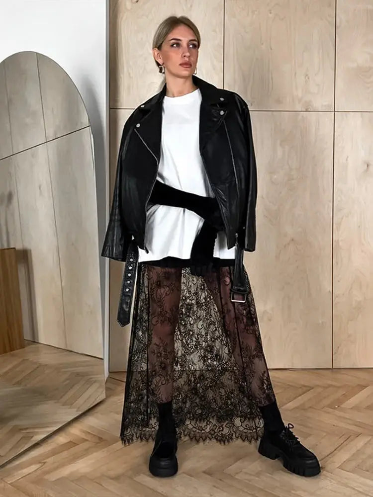 Person wearing a black leather jacket, white top, and patterned skirt in a modern interior setting.