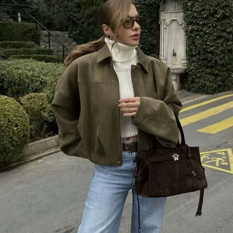 Woman in a green jacket and white turtleneck with a brown bag on a street.