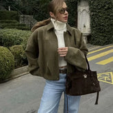 Woman in a green jacket and white turtleneck with a brown bag on a street.