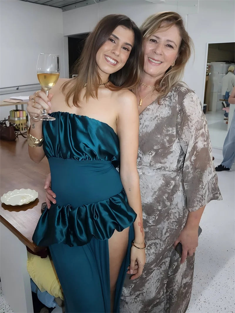 Two women posing together, one in a teal dress holding a glass of wine, in an indoor setting.