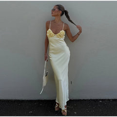 Woman in a white dress with floral straps against a plain wall