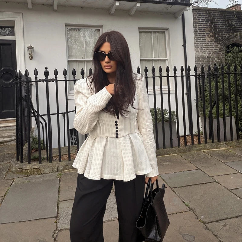 Woman wearing a white peplum top and black pants standing on a sidewalk.