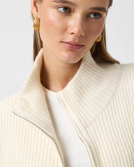 Woman wearing a cream ribbed sweater over a white shirt with a plain background