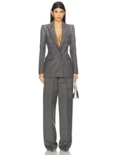 Model wearing a grey crystal-embellished blazer and matching wide-leg pants, holding a silver handbag.