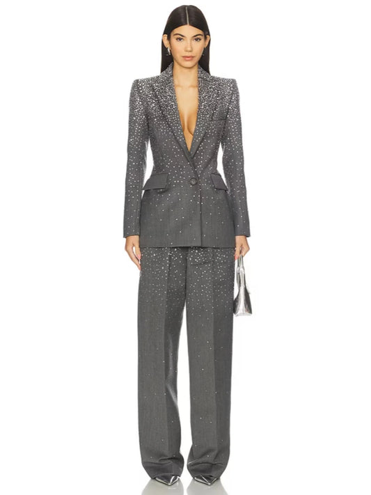 Model wearing a grey crystal-embellished blazer and matching wide-leg pants, holding a silver handbag.