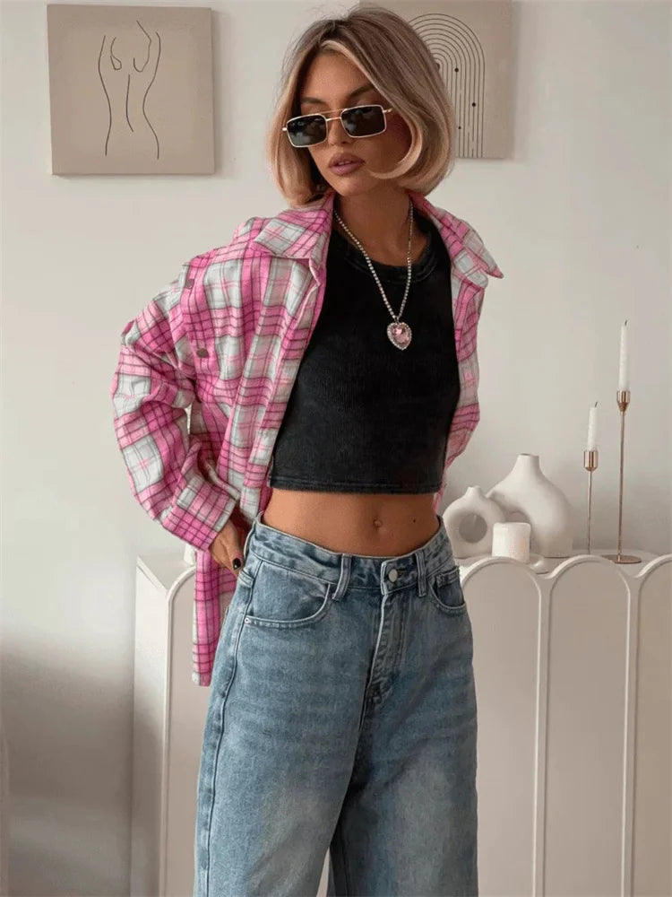 Woman wearing a pink plaid shirt, black top, and blue jeans indoors.