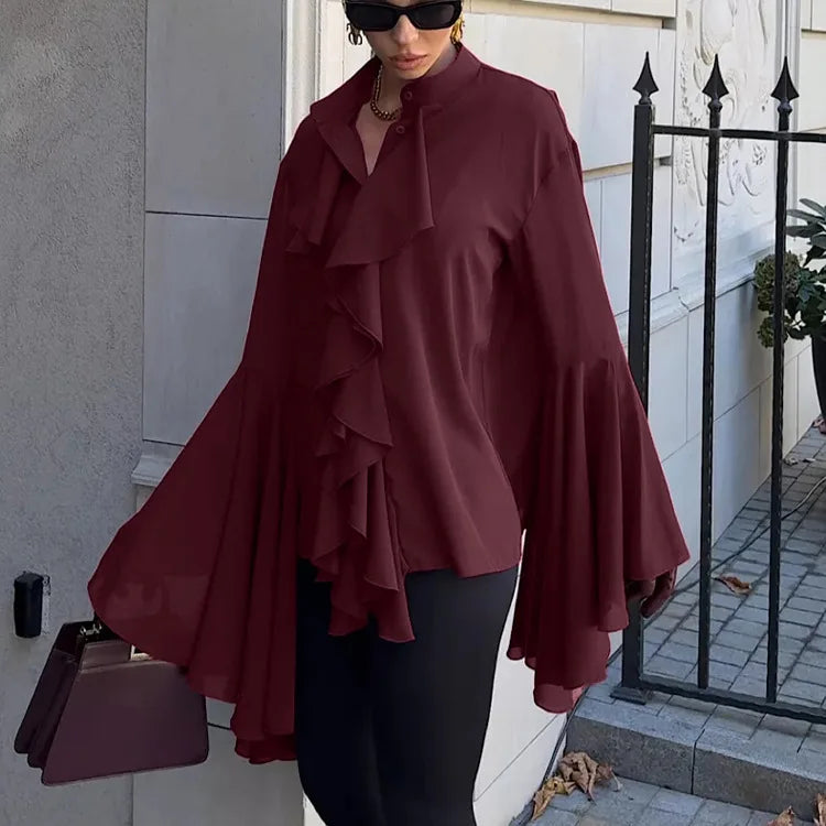 Woman wearing a burgundy ruffled blouse and black pants, standing outdoors.