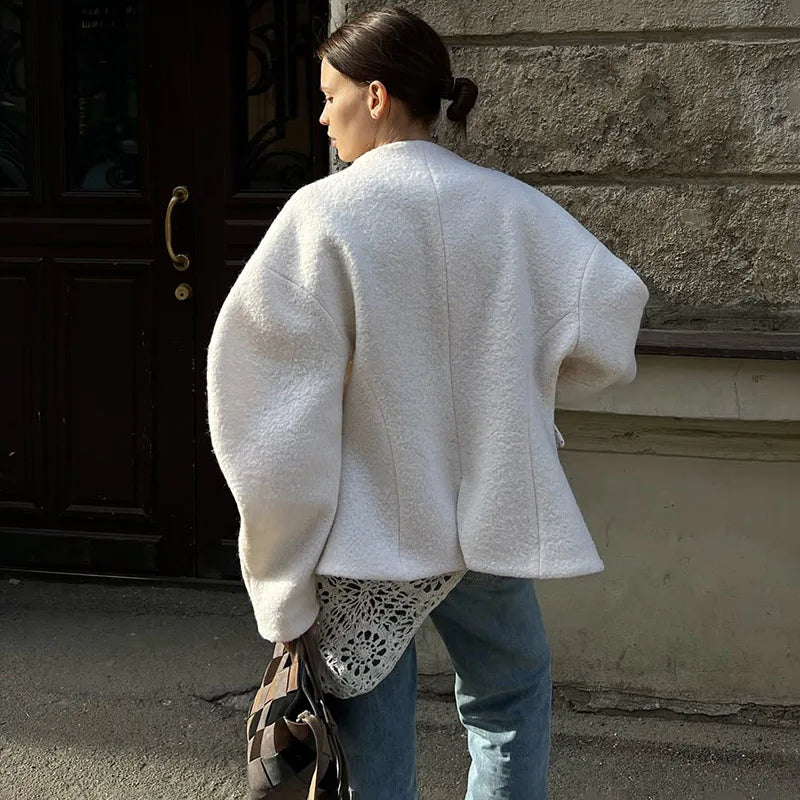 Woman wearing a white oversized sweater and blue jeans against a textured wall.