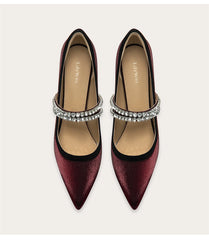 Pair of maroon high-heeled shoes with silver ankle straps on a light beige background