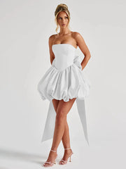 Woman wearing a white strapless dress with a high-low hem on a plain background