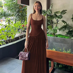 Woman in a brown dress holding a purple handbag in an outdoor setting with plants.