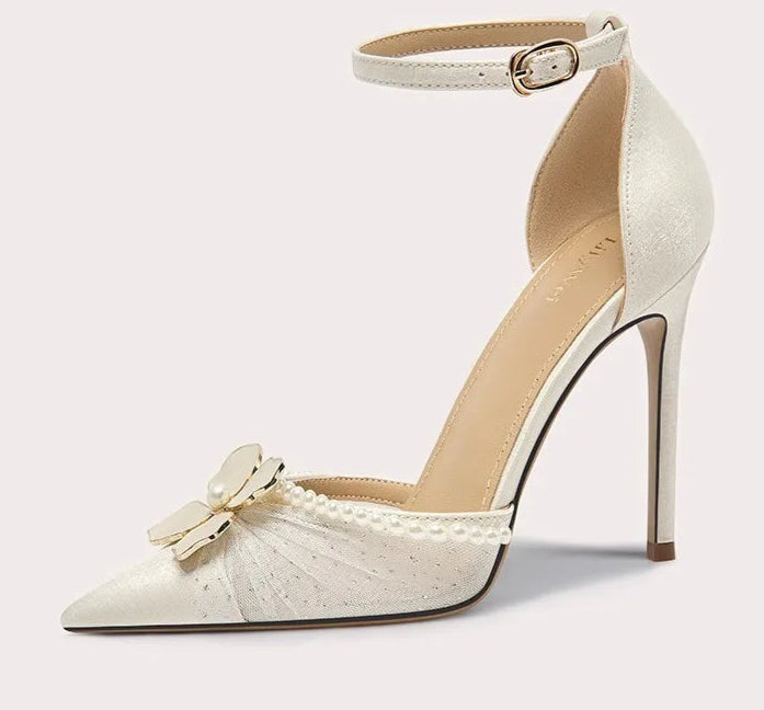White high-heeled shoe with decorative bow and pearls on a light gray background