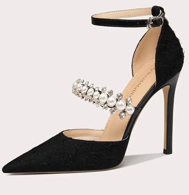 Black high-heeled shoe with pearl embellishments on a light gray background