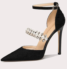 Black high-heeled shoe with pearl embellishments on a light gray background