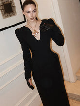 Woman in a black dress with cut-out design and gloves standing indoors.