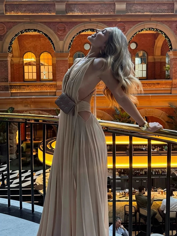 Woman in a long dress standing in an elegant interior setting with arched windows.