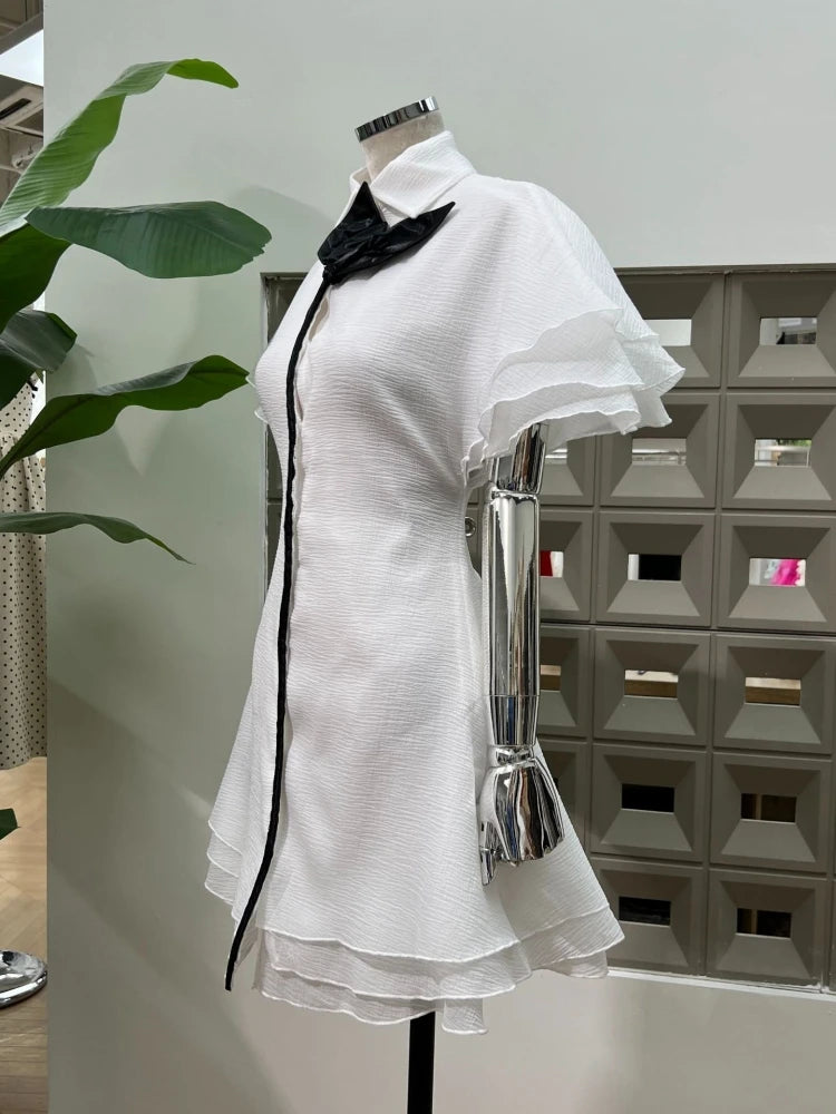 White dress with black trim on a mannequin against a geometric wall.