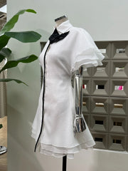 White dress with black trim on a mannequin against a geometric wall.