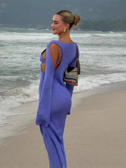Woman in a blue dress standing on a beach with ocean waves in the background