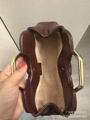 Brown handbag with gold handles held by a hand