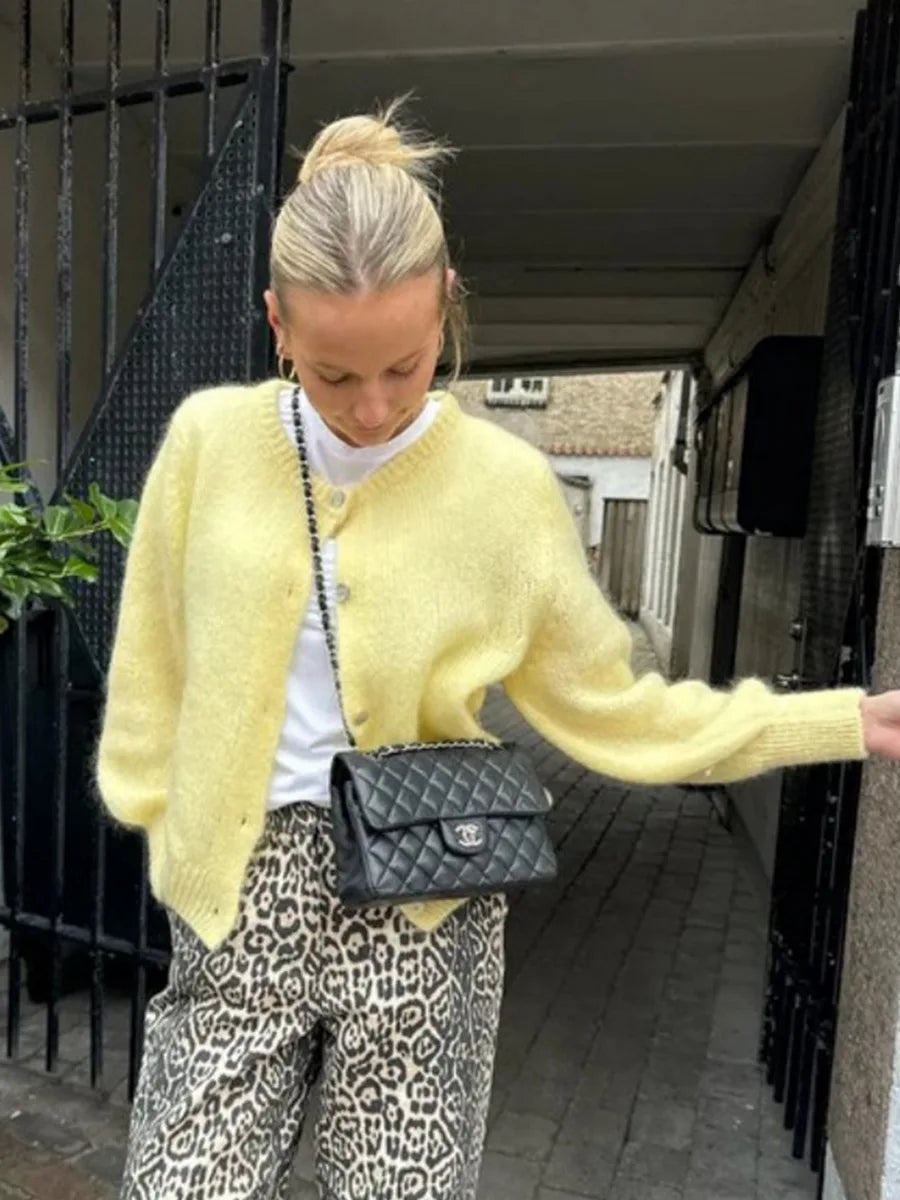Person wearing a yellow cardigan, white shirt, and leopard print pants, holding a black handbag.