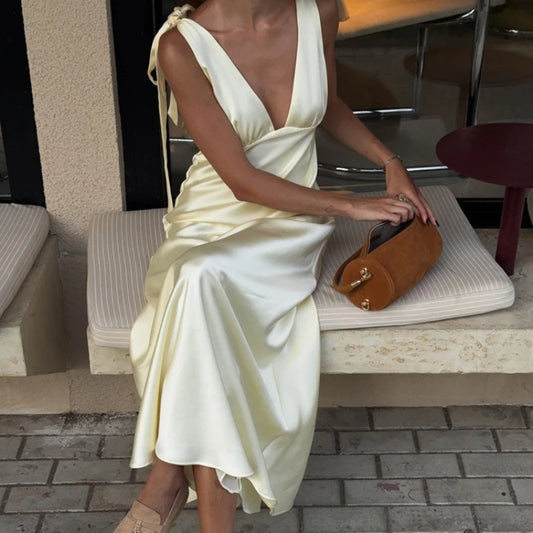 Woman in a white dress sitting on a bench with a brown handbag.