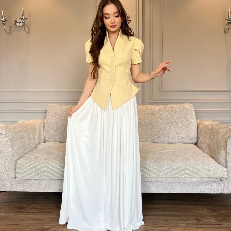 Woman in a yellow top and white skirt standing in a room with a gray sofa.
