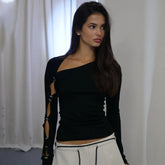 Woman wearing a black long-sleeve top with cut-out design and white pants against a plain background