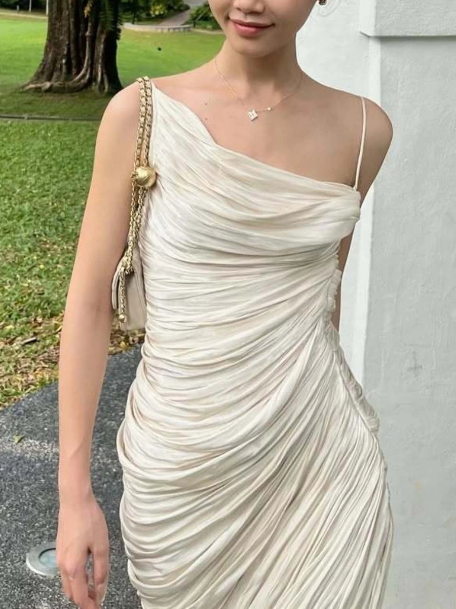 Woman wearing a white one-shoulder dress with a gold handbag outdoors.