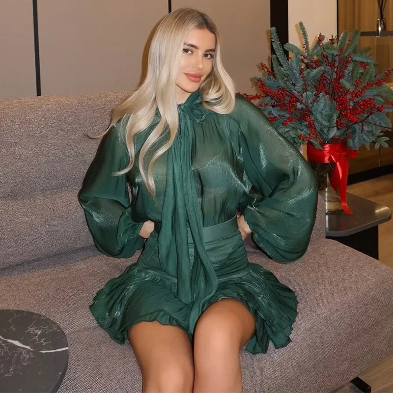 Woman in a green dress sitting on a couch with a decorative plant in the background