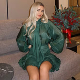 Woman in a green dress sitting on a couch with a decorative plant in the background