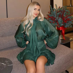 Woman in a green dress sitting on a couch with a decorative plant in the background