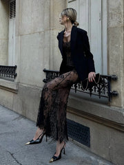 Woman in black outfit with sheer skirt sitting on a bench against a building.