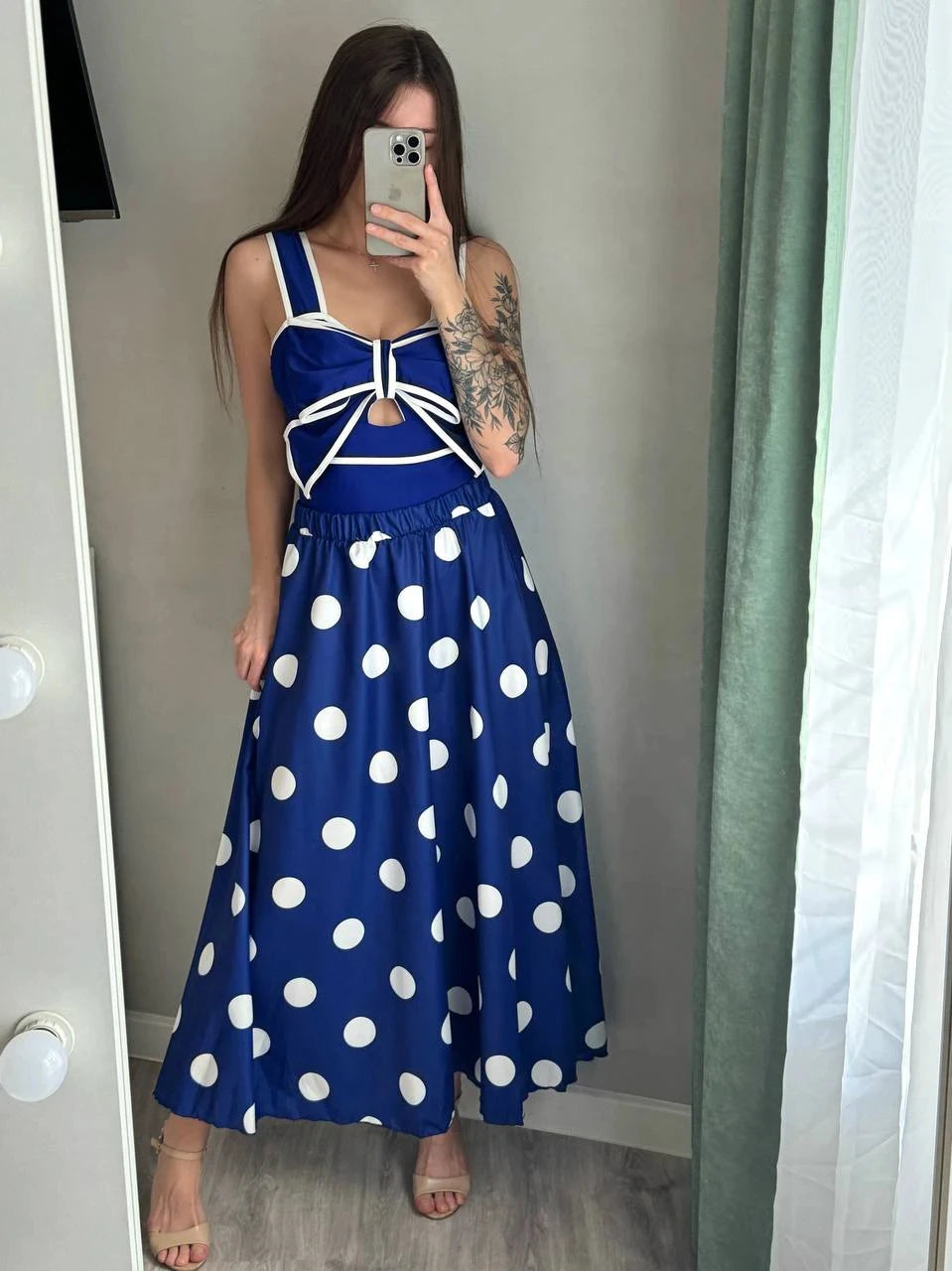 Woman wearing a navy blue polka dot tankini swimsuit with a bow detail and a matching A-line skirt, standing in front of a mirror.