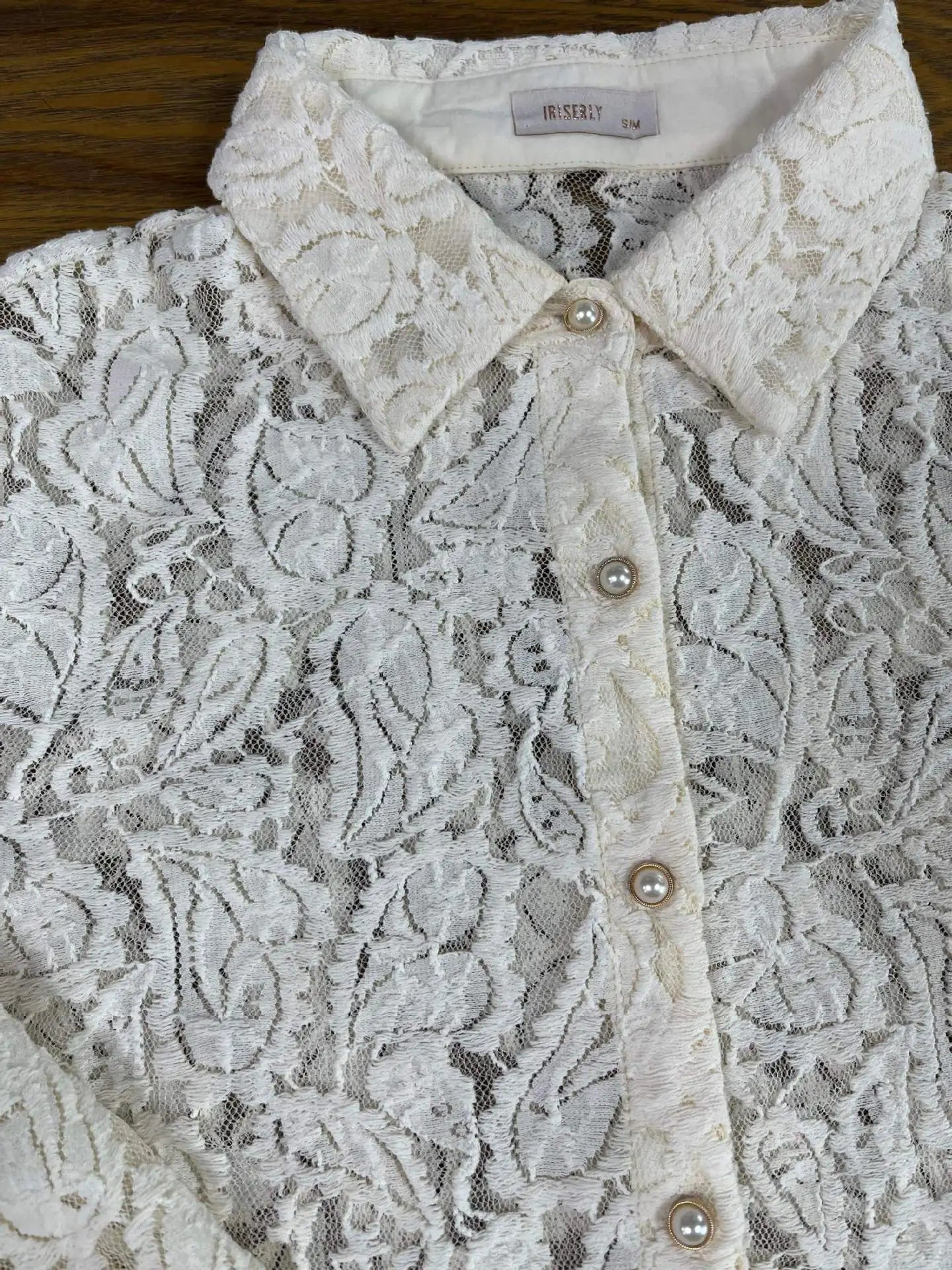 Close-up of a lace blouse with a brand label on a wooden surface