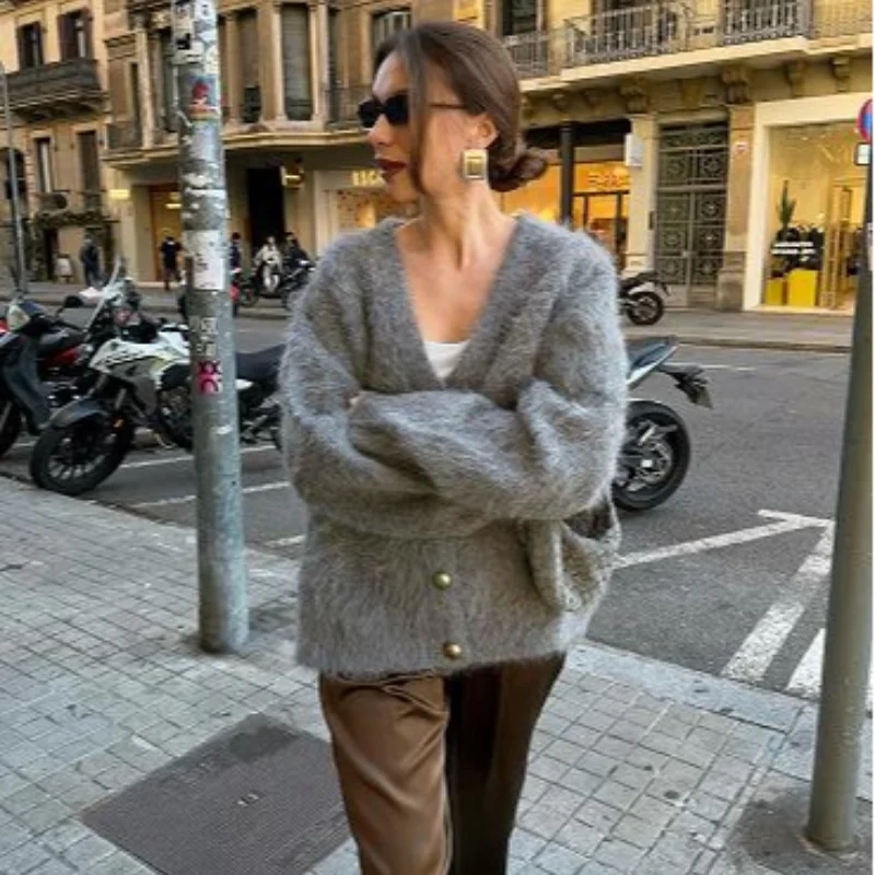 Woman wearing a gray cardigan on a city street with motorcycles and buildings in the background.