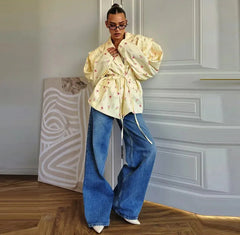 Person wearing a light-colored floral blouse and blue jeans in an indoor setting.