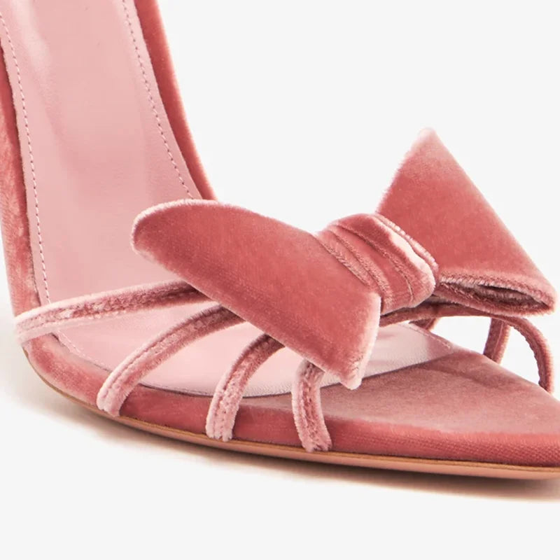 Feet wearing pink velvet bow detail thin heel sandals