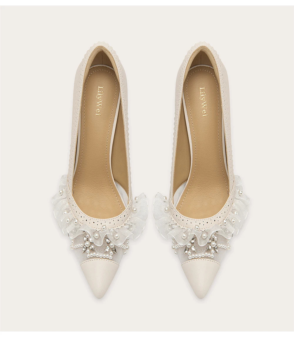 White pointed-toe shoes with lace and pearl details on a white background