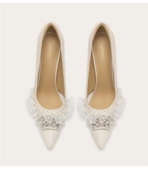 White pointed-toe shoes with lace and pearl details on a white background