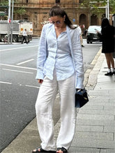 Woman in a light blue blazer and white pants walking on a city street.
