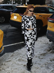 Person wearing a black and white floral outfit standing in a snowy street with yellow taxis in the background.