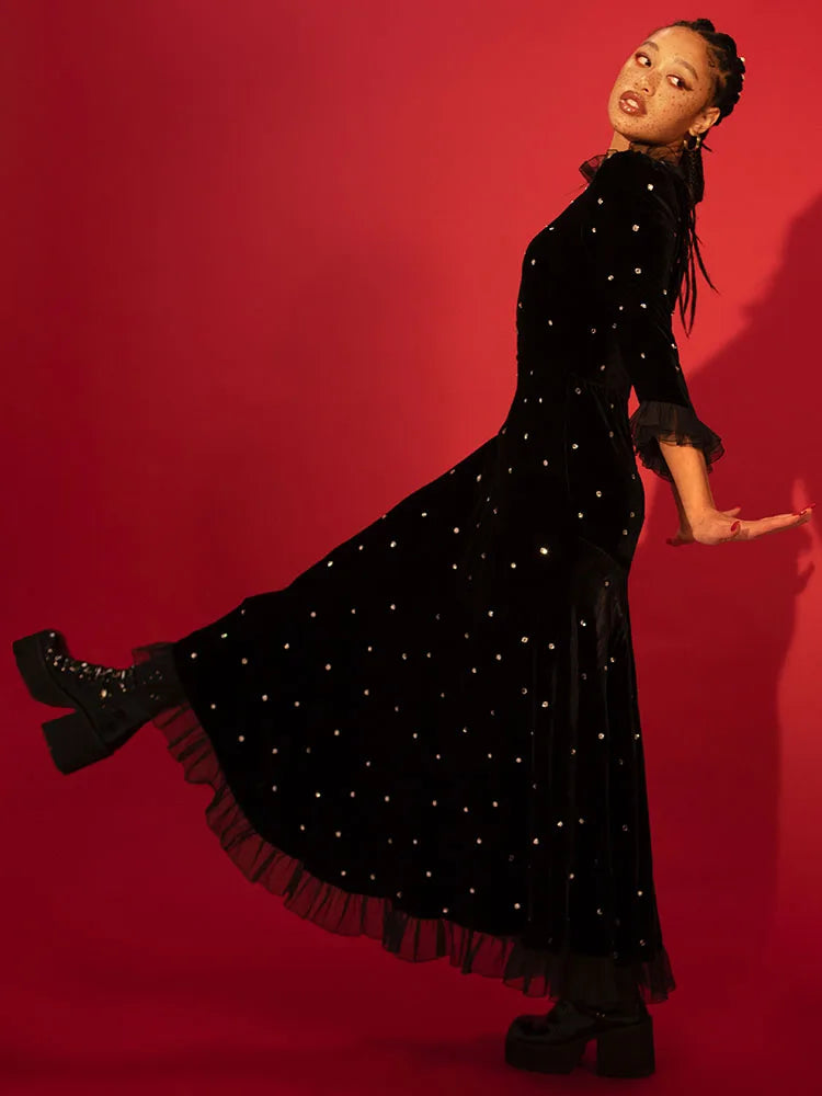 Woman in a black dress with white embellishments against a red background