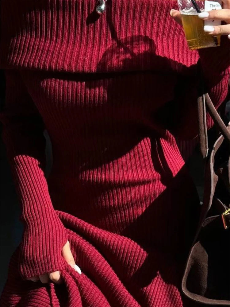 Person wearing a red ribbed sweater holding a glass of beer.
