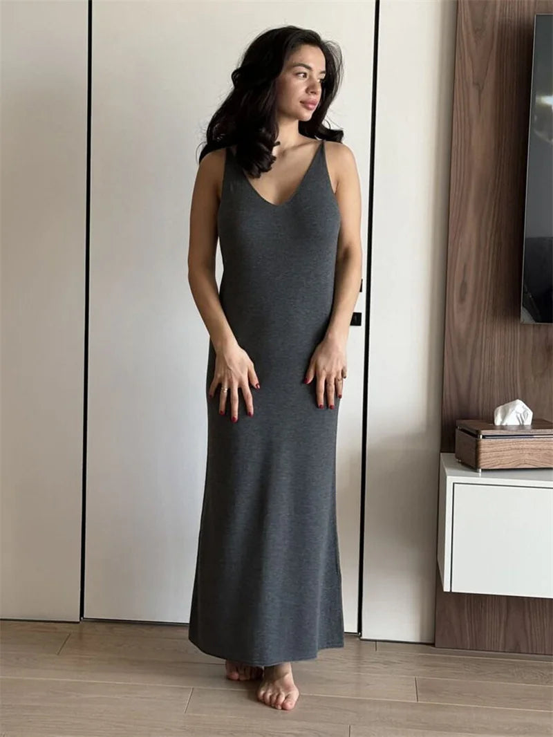 Woman wearing a gray sleeveless dress standing in a room with wooden flooring and a white wall.