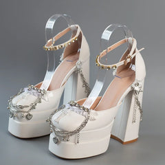 White high-heeled shoes with decorative straps and charms on a gray background