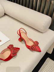 Red high-heeled shoes with decorative bows on a beige sofa.