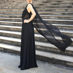 Woman in a black dress with a flowing cape standing on stone steps.